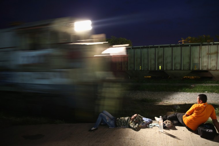 Two Central American immigrants wait for a train to climb aboard.