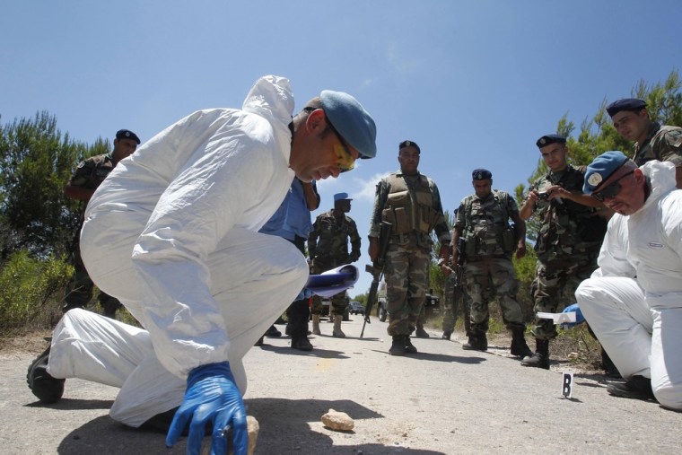 Scientific investigators -- part of the U.N. peacekeeping force in south Lebanon -- inspect the area near an explosion that injured four Israeli soldiers close to the Israel-Lebanon border as Lebanese Army soldiers watch.