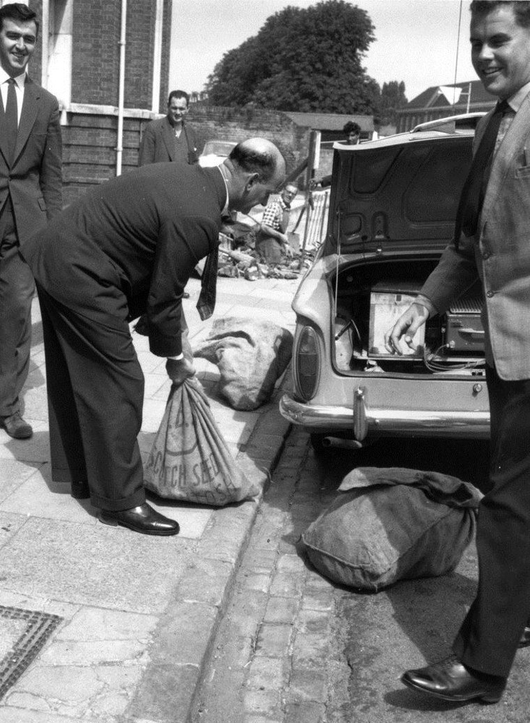 Police officers put bags of evidence into a car trunk in August 1963.