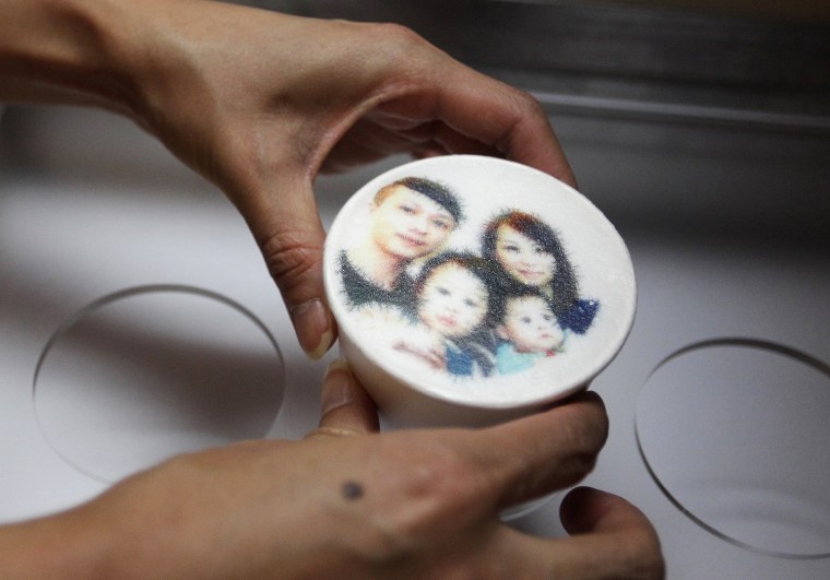 An employee holds a latte with a customer's picture printed on top of the milk foam at a Family Mart in Taipei on Aug. 13, 2013