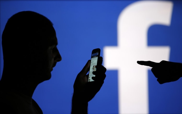 A man is silhouetted against a video screen with an Facebook logo as he poses with an Samsung S4 smartphone in this photo illustration taken in the ce...