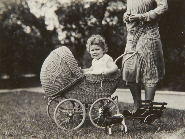 A 2-year-old Princess Elizabeth poses for the camera while sitting in a wicker pram in 1928. The photos were taken by her father, King George VI when he was the Duke of York.