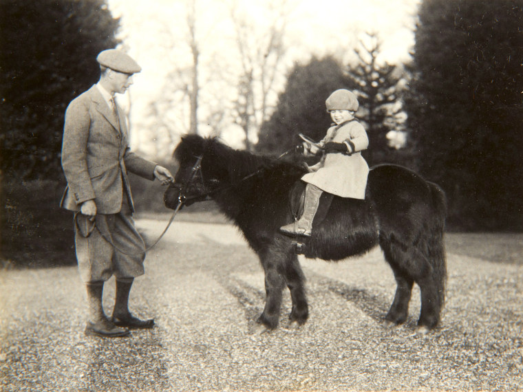 A 4-year-old Princess Elizabeth her Shetland pony named Peggy while her father King George VI, then the Duke of York stands next to her. The photo was taken by her mother Queen Elizabeth when she was the Duchess of York.