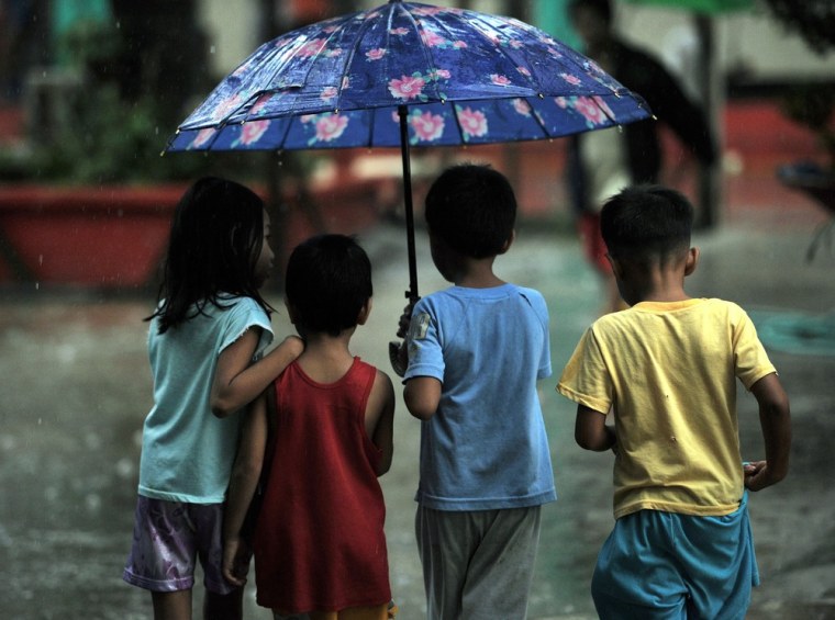 Children affected by flooding due to heavy rains exacerbated by Tropical Storm Trami share an umbrella after receiving free donuts at a school building serving as an evacuation center in Marikina, east of Manila on Aug. 21.