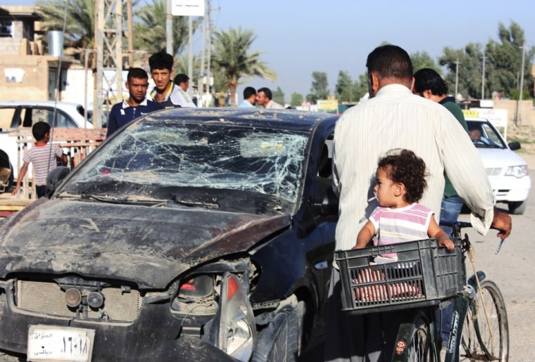 Residents pass by a damaged vehicle a day after a bomb attack in central Baquba, 40 miles northeast of Baghdad, August 25, 2013.