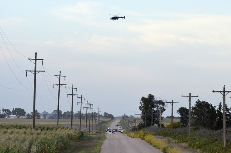 Law enforcement officials gather on a county road northwest of Imperial, Neb., early Sunday as a Nebraska State Patrol helicopter scours nearby corn fields for a kidnapping suspect.