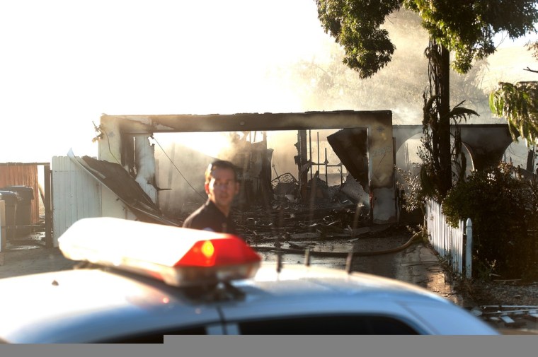 A police officer stands outside one of several scorched homes.