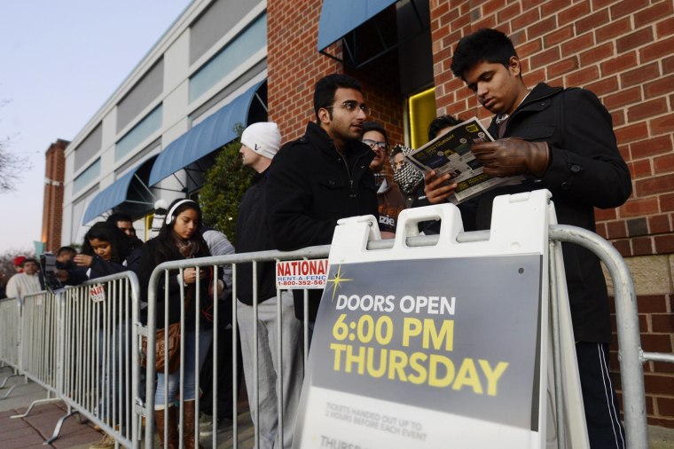 Shoppers check out a list of sale items while waiting in a line for a Best Buy to open on Thanksgiving Day in Alexandria, Va.
