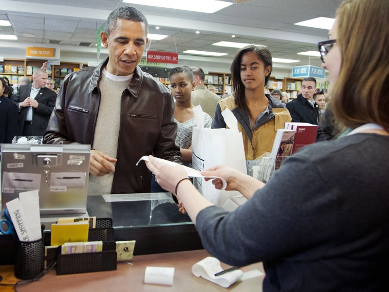 President Barack Obama, with daughters Sasha, center, and Malia, pays for his purchase the the local bookstore Politics and Prose in northwest Washing...