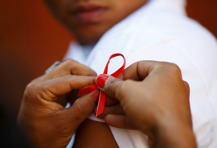 A red ribbon is put on the sleeves of a man by his friend to show support for people living with HIV during a program to raise awareness about AIDS on...