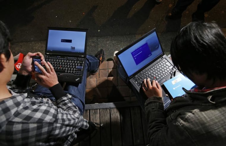 Men install Microsoft Corp's Windows 8 operating system on their laptops, as Windows 8 goes on sale after midnight, along a street at the Akihabara di...