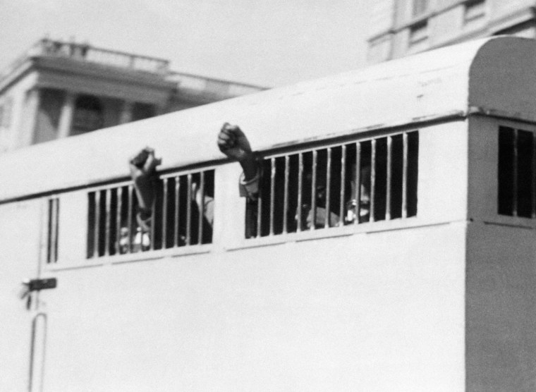 Eight men, among them anti-apartheid leader and African National Congress (ANC) member Nelson Mandela, sentenced to life imprisonment in the Rivonia trial leave the Palace of Justice in Pretoria 16 June 1964 with their fists raised in defiance through the barred windows of the prison car.