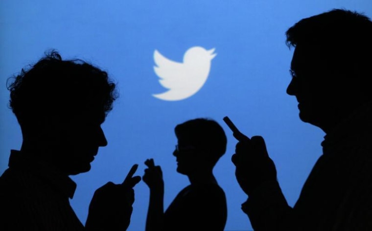 People holding mobile phones are silhouetted against a backdrop projected with the Twitter logo in this illustration picture taken in Warsaw September...