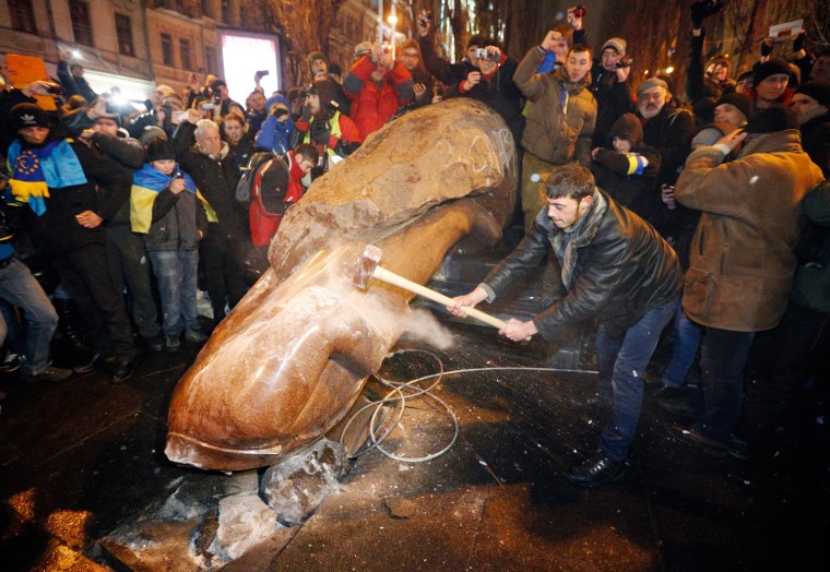 A protester hammers at a statue of former Soviet leader Vladimir Lenin as others gather around after it was toppled during a pro-European protest in downtown Kiev, Ukraine, Dec. 8, 2013.