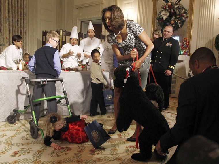 U.S. first lady Michelle Obama reacts as two year old Ashtyn Gardner from Mobile, Alabama, trips over another child's walker after meeting Obama's new dog Sunny at the unveiling of the decorations at the White House in Washington, December 4, 2013.