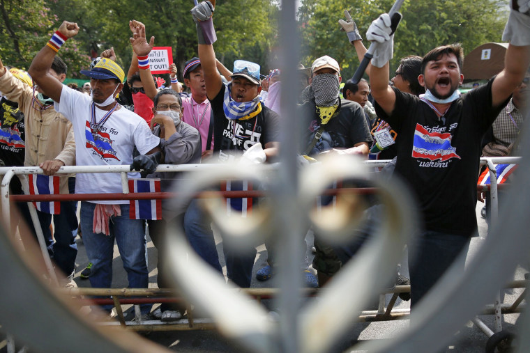Anti-government protesters gesture from behind gates of the compound of the prime minister's office, known as the Government House, after a small group of them removed barbed wire installed by police in Bangkok on Thursday.