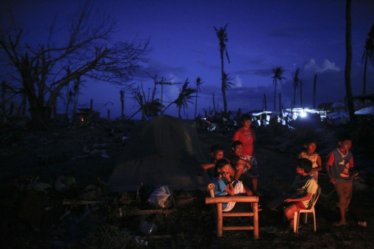 Survivors of Typhoon Haiyan sit near a fire, amid the ruins of their destroyed neighborhood, as night falls in Tacloban City on Nov. 24, 2013.