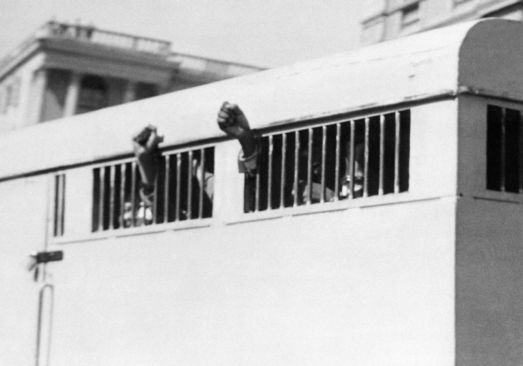 Eight men, among them anti-apartheid leader and member of the ANC Nelson Mandela, sentenced to life imprisonment in the Rivonia trial, leave the Palace of Justice in Pretoria 16 June 1964 with their fists raised in defiance through the barred windows of the prison car.