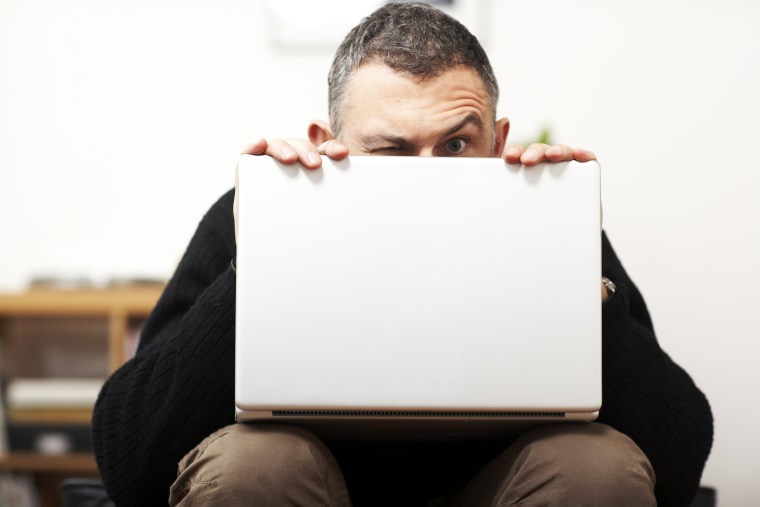 Man making faces from behind laptop; stock photography; computer; suspicious; raised eyebrow