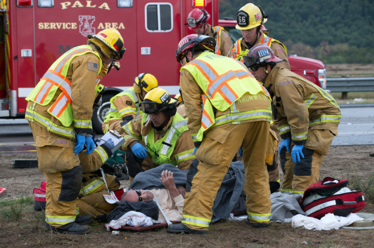 Firefighters and paramedics tend to a victim after a tour bus overturned on rain-slick Interstate 15 near Fallbrook, Calif., in San Diego County Thursday afternoon, Dec. 19, 2013.
