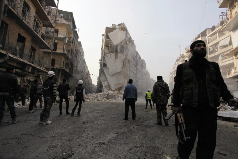 A Free Syrian army fighter and others look at damage caused by what activists said was an airstrike with explosive barrels by forces loyal to President Bashar al-Assad in Al-Shaar area in Aleppo on Dec. 17, 2013.