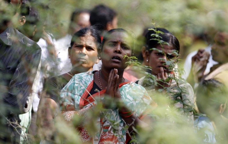 An Indian woman watches with folded hands as hospital staff and volunteers carry charred bodies of passengers near the site of a train fire about 100 miles north of Bangalore, India, on Saturday. A fire engulfed two coaches of an express train in southern India early Saturday, killing at least 23, many of whom became trapped and suffocated after the doors failed to open, officials said.