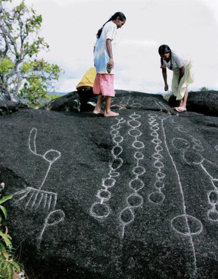 Two Wapishana women maintain traditional rock carvings at a spiritual site.
