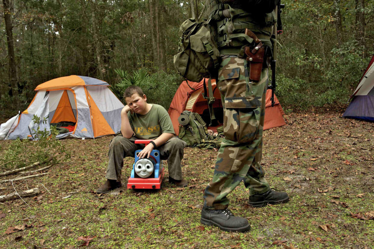 A young boy sits on a toy, upset because his sister got to carry the rifle that he wanted.