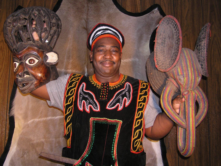 African-American genealogist William Holland, dressed in traditional garb, shows off the ceremonial masks he bought on eBay. He plans to return the masks to the tribes from whence they came during a trip to Cameroon this month.