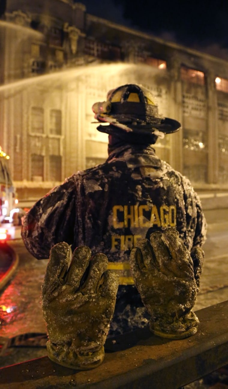 An ice-covered pair of gloves belonging to a Chicago firefighter stand on a railing behind him in single-digit temperatures during a five-alarm blaze in the city's Bridgeport neighborhood on Jan. 23, 2013.