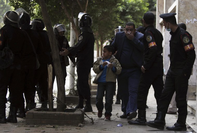 A man walks past riot police as he covers his face from tear gas during clashes with protesters opposing Egyptian President Mohamed Mursi, along Simon Bolivar Square, which leads to Tahrir Square, in Cairo Jan. 30, 2013. Egyptian President Mohamed Mursi flew to Germany on Wednesday to try to convince Europe of his democratic credentials, leaving behind a country in crisis after a week of violence that has killed more than 50 people.