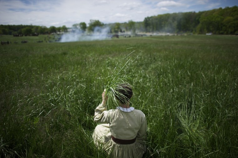 With a makeshift parasol of tall grasses, Brittney Mumma, 17, of the Civil War Civilians of Spotsylvania, observes the Chancellorsville 150th reenactment from a distance on May 4, 2013 in Chancellorsville, VA.