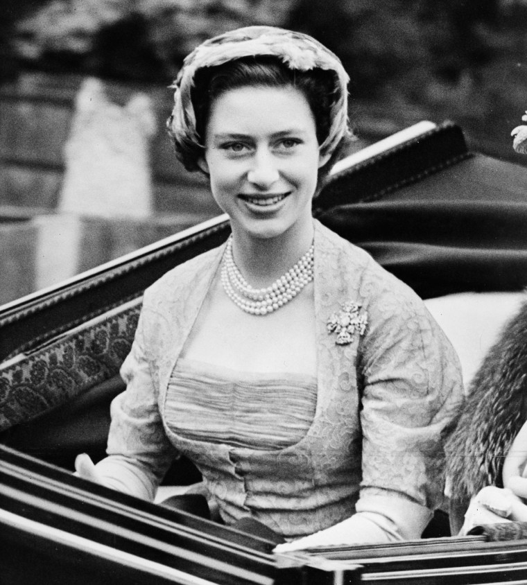 Princess Margaret wears a 1952 gray lace dress by Norman Hartnell. The boned fitted bodice is intricately constructed in layers of grey silk net with grey leaf-patterned lace underneath.