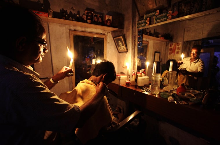 An Indian barber holding a candle, has a haircut for a customer at his shop in Kolkata, India, Tuesday, July 31, 2012. India's energy crisis cascaded...