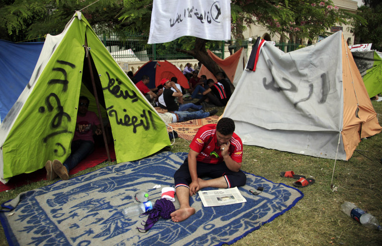 An opponent of Egypt's Islamist President Mohammed Morsi reads a newspaper at his tent with Arabic writing that reads,
