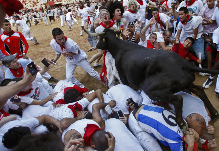 A cow jumps over revelers lying down on the bull ring as one of them is pushed by the animal on July 11.
