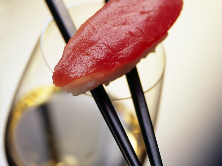 A piece of salmon and rice on two chopsticks laying on a glass of white wine