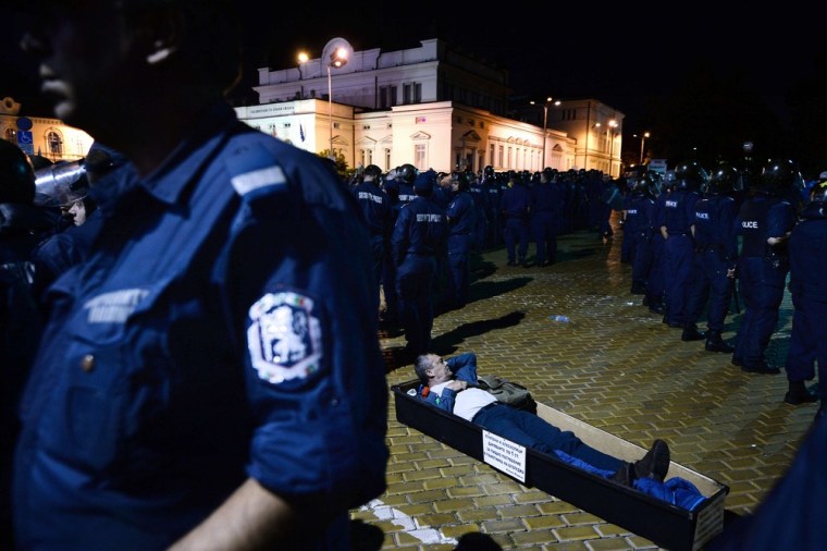 A protester lies in a coffin in front of riot policemen making way for lawmakers and parliament staff leaving the parliament building early on July 24.
