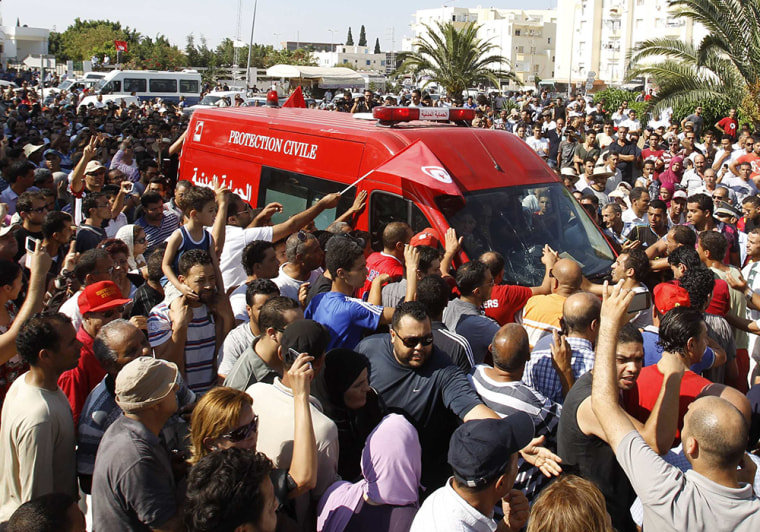 People walk beside the ambulance carrying the body of assassinated Tunisian opposition politician Mohamed Brahmi in Tunis Thursday.