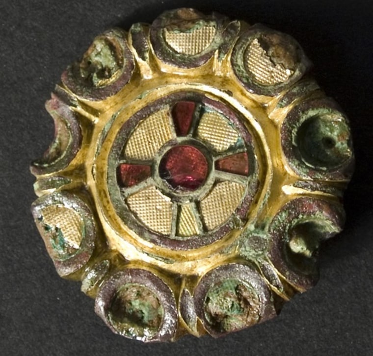 This brooch appears to be from continental Europe and contains gold textured in a waffle shape along with a cross made of red glass and semiprecious s...