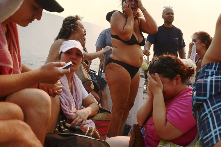 Tourists and locals are seen on board a small boat as a wildfire approaches the village of Megalo Livadi on July 27.