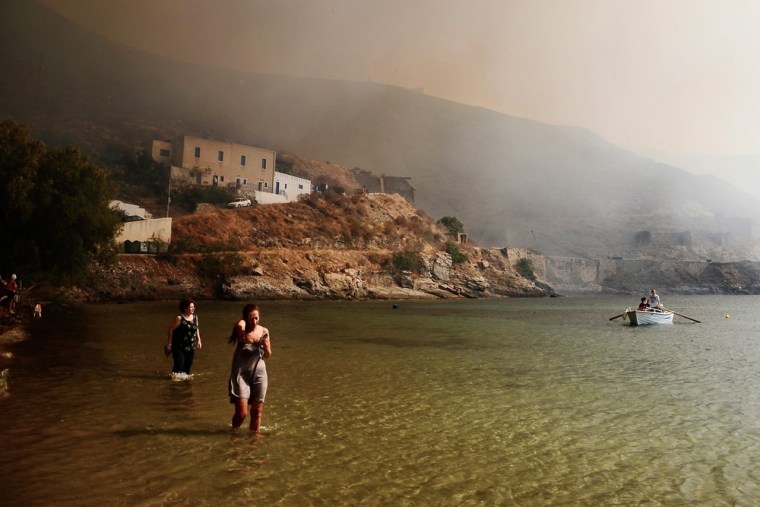 People walk in the sea as a wildfire approaches the village of Megalo Livadi on July 27.