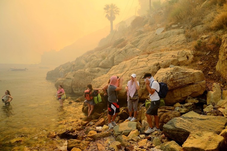 Tourists and locals finding shelter near the seaside as a wildfire approaches the village of Megalo Livadi on Serifos island on July 27.