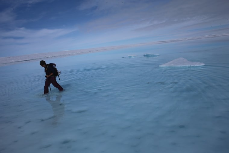 Sarah Das from the Woods Hole Oceanographic Institution walks though a surface meltwater lake on July 16 on the Glacial Ice Sheet, Greenland. She is part of a team of scientists that is using Global Positioning System sensors to closely monitor the evolution of the surface lakes and the motion of the surrounding ice sheet.