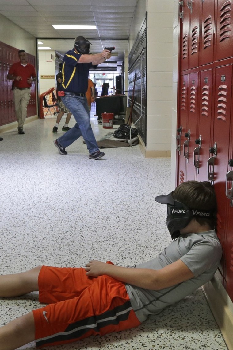 In this photo taken July 11, a Clarksville schools faculty member, wearing a protective mask, rear center, carries a practice handgun toward a classroom in the city's high school in Clarksville, Ark.