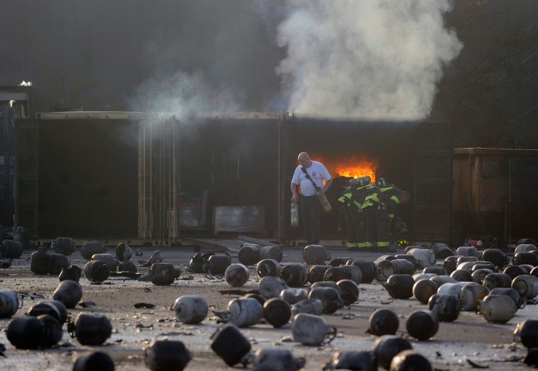 Firefighters prepare to put out a container of burning caps, as thousands of exploded propane cylinders litter the storage yard of a propane plant, after massive explosions overnight in the plant's yard, in Tavares, Fla., on July 30. Dozens of explosions rocked a propane tank servicing plant in central Florida, northwest of Orlando, late on Monday, injuring eight people, at least three critically, and prompting the evacuation of nearby homes, authorities said.