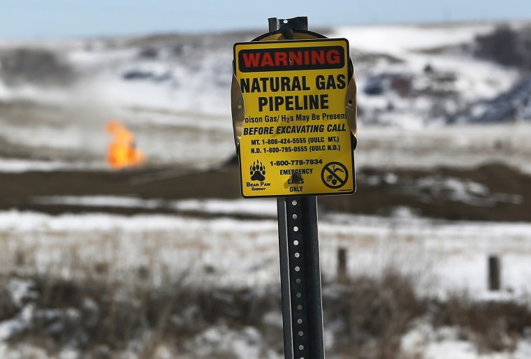 A warning sign for a natural gas pipeline is seen in front of natural gas flares at an oil pump site outside of Williston, North Dakota in this March ...
