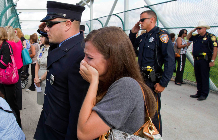 A woman grieves as firefighters and police officers salute as they watch the procession during a memorial service for four Houston firefighters on June 5.