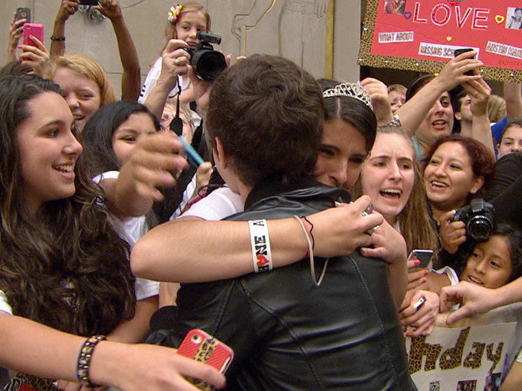 A girl in a tiara hugs Mahone on the plaza.