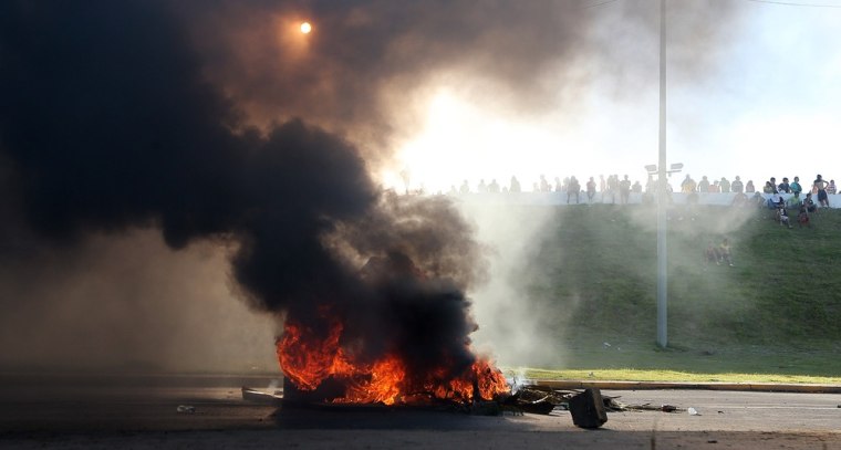 Protestors line a highway barrier in front of a burning barricade of tires near the Castelao stadium in Fortaleza, Brazil, Wednesday, June 19, 2013. Protesters cut off the main access road to the stadium where Brazil goes up against Mexico in the Confederations Cup soccer tournament. Beginning as protests against bus fare hikes, demonstrations have quickly ballooned to include broad middle-class outrage over the failure of governments to provide basic services and ensure public safety.